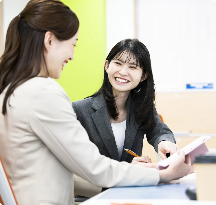 オフィスで資料を広げ, 明るい笑顔で打ち合わせをするスーツ姿の女性社員