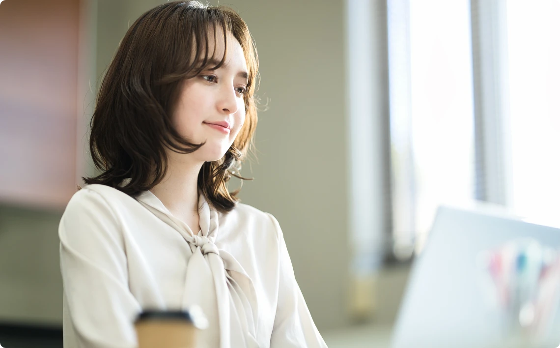 明るいオフィスで集中してパソコン作業を行う、きれいめオフィスカジュアルの女性
