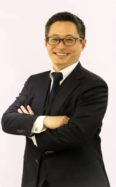 高層ビルを背景に、腕を組んで爽やかな笑顔を見せるメガネをかけた男性ビジネスマン