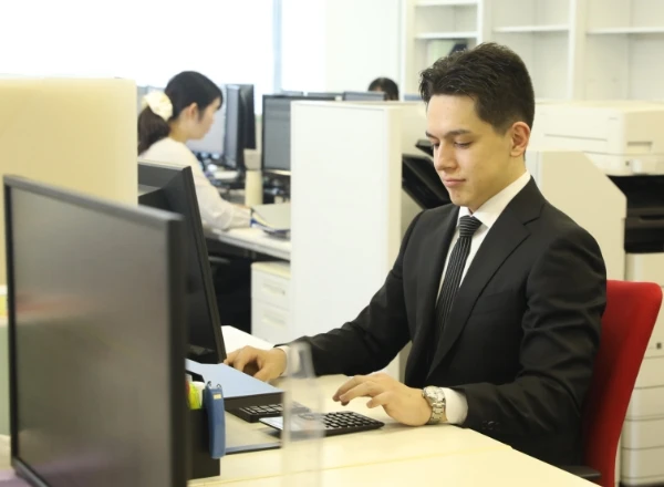 活気のあるオフィスで、デスクに向かって集中して仕事に取り組むスーツ姿の男性社員