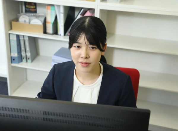 パソコン画面の前で、落ち着いた表情で業務を行うスーツ姿の女性社員