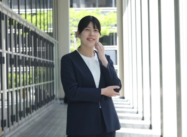 光が差し込むオフィスの通路で、笑顔で佇むスーツ姿の女性社員