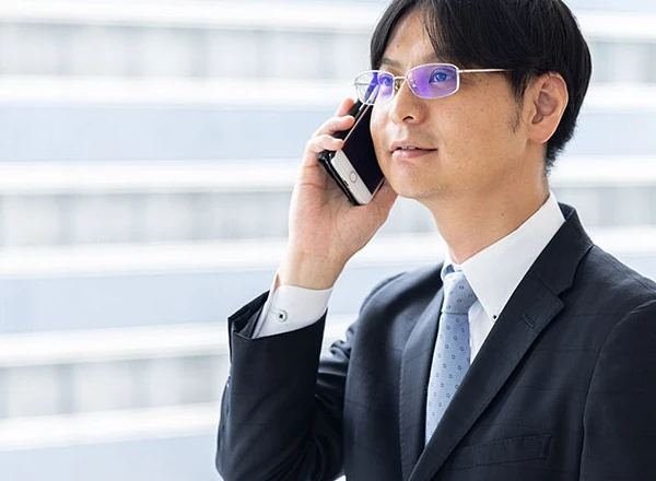 屋外でスマートフォンでの通話に集中する、スーツにメガネ姿の男性ビジネスマン