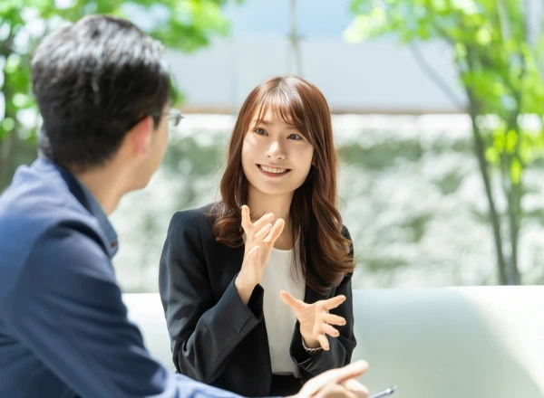 緑のある屋外で、身振り手振りを交えて楽しそうに打ち合わせをする女性社員