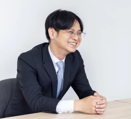 オフィスでデスクに座り、笑顔で話すスーツ姿の男性社員