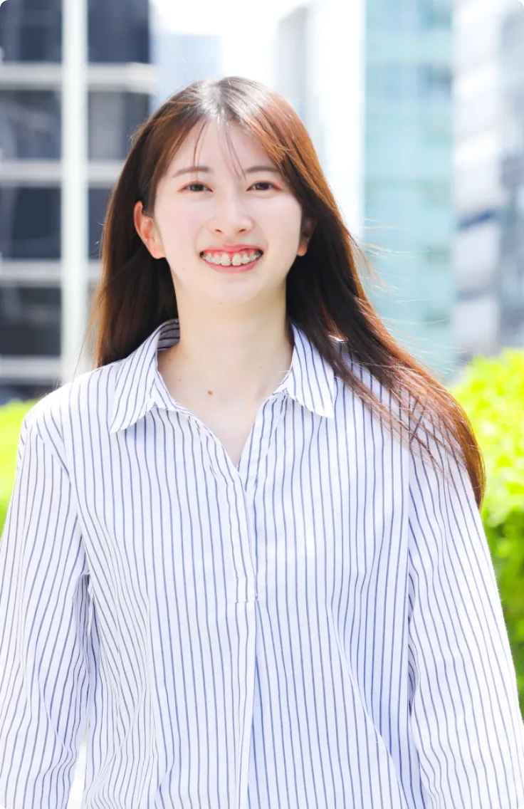 ストライプのシャツを着て、屋外で爽やかな笑顔を見せるロングヘアの女性社員