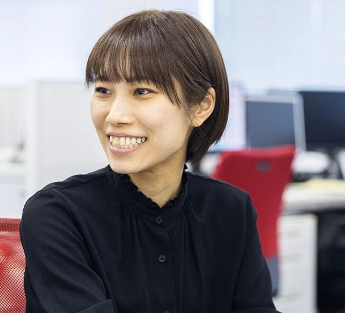 オフィスのデスク席で明るい笑顔を見せる髪の短い女性社員