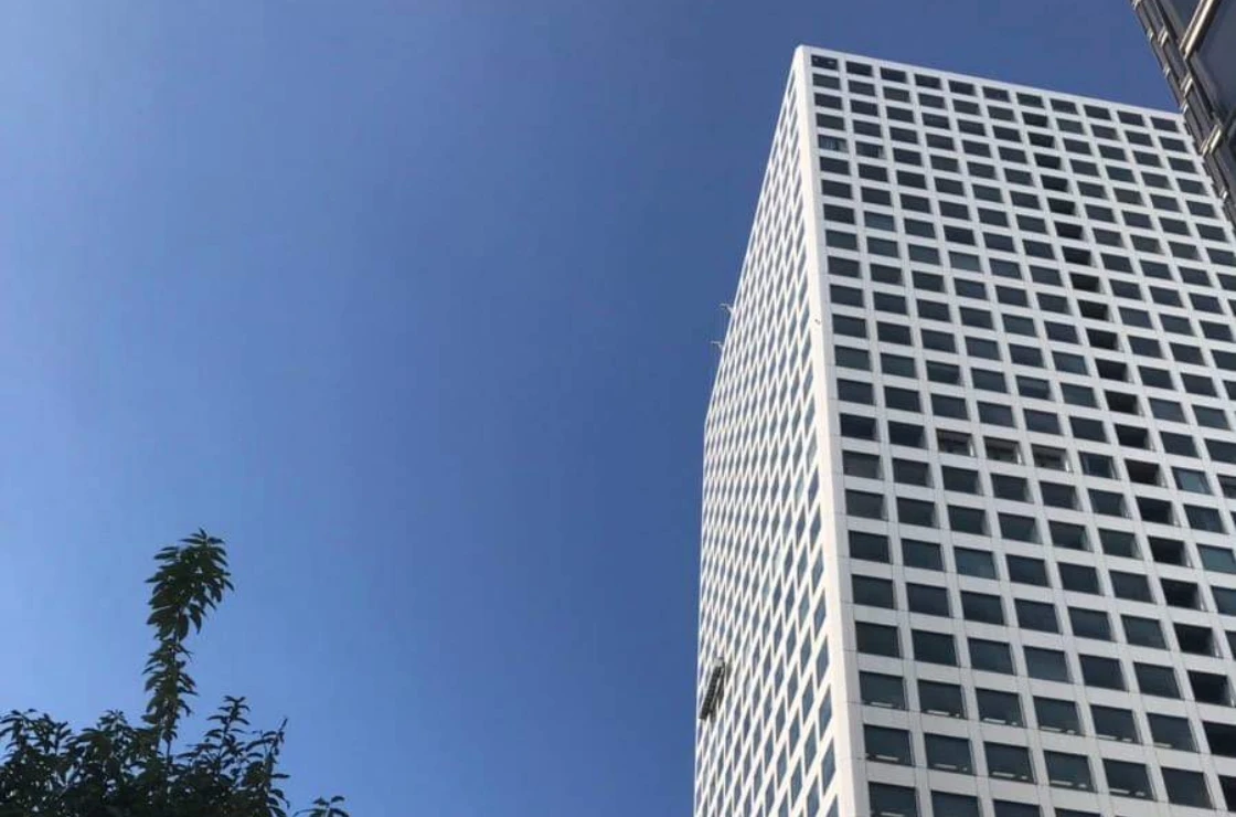 青空を背景に、真下から見上げた正方形の窓が規則的に並ぶ白い高層オフィスの外観